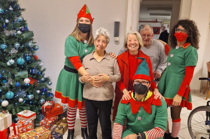 Foto di gruppo di alcuni ospiti e collaboratori vestiti da elfi, vicino ad un albero di Natale con vari regali